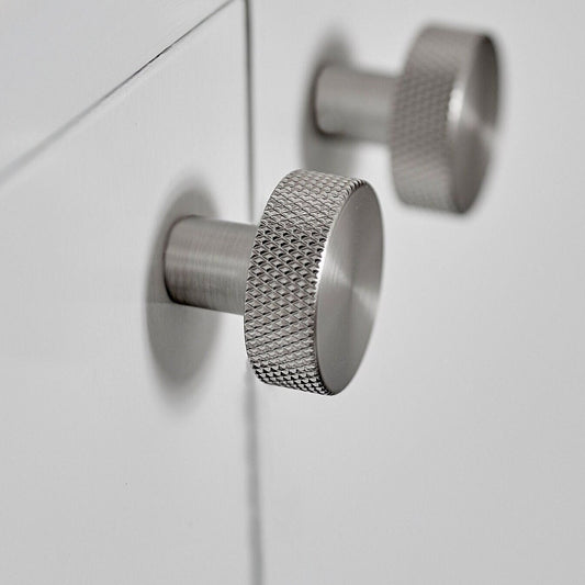 May include: Two silver cabinet knobs with a textured, diamond-shaped pattern. The knobs are round and have a cylindrical stem.